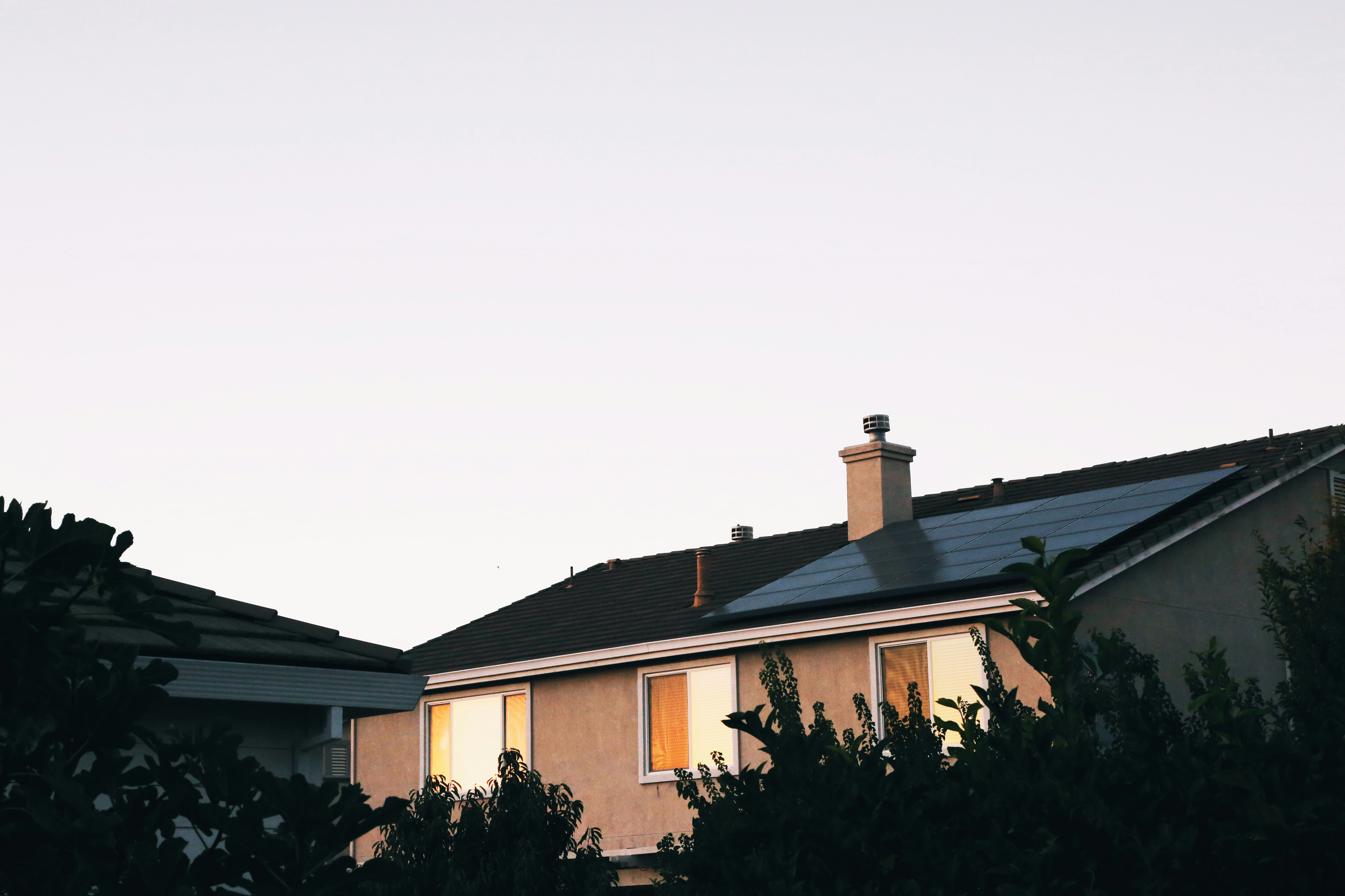 Maison individuelle avec panneaux solaires photovoltaïques en toiture, fenêtres éclairées à la tombée du jour